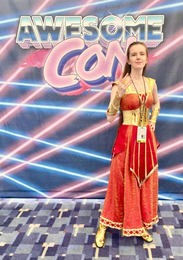 Photo of Riverly Twardy at Awesome Con 2026, wearing her Kyndara cosplay, standing in front of a banner that reads "Awesome Con".