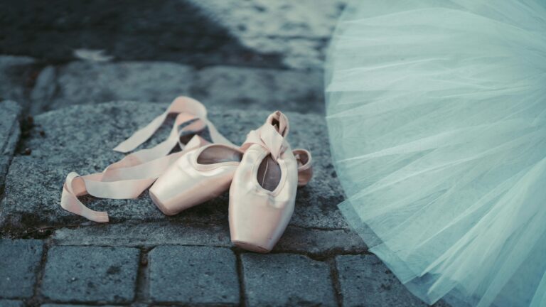 Close-up of ballet pointe shoes on cobblestone with a blue tutu, emphasizing elegance and grace.