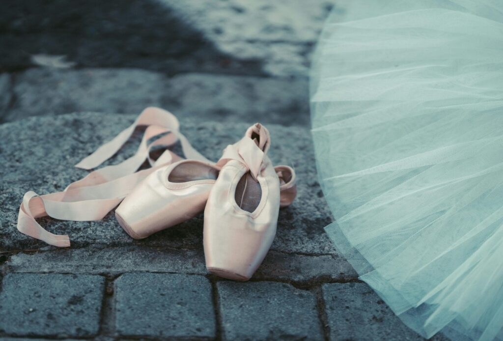 Close-up of ballet pointe shoes on cobblestone with a white tutu, emphasizing elegance and grace.