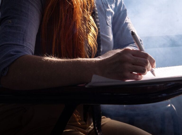 Close-up of a student concentrating on taking notes in a classroom setting with dramatic lighting.